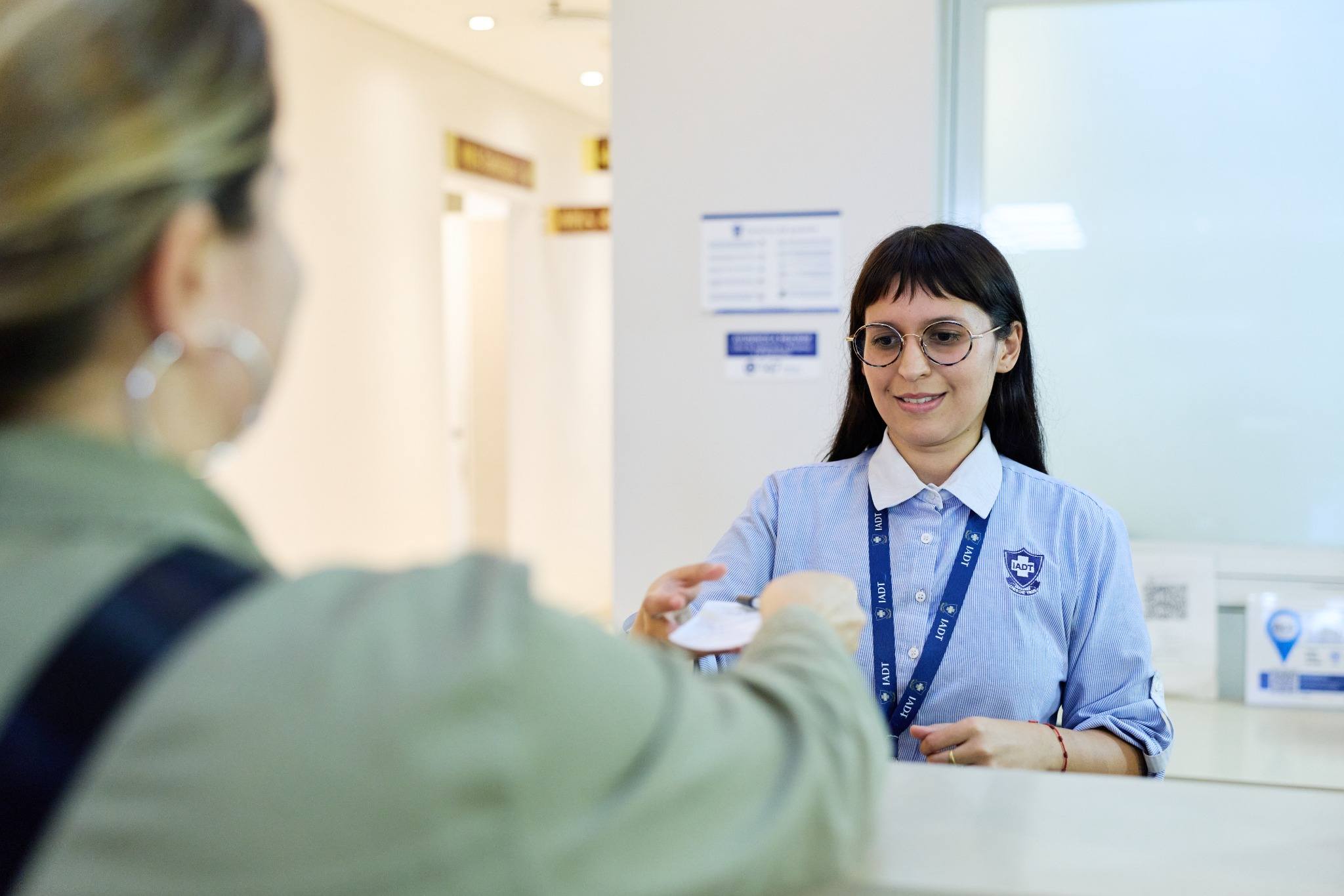 Personal administrativo del IADT entregando documentación a una paciente en el área de recepción
